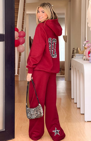 A pair of red wide-leg sweatpants featuring a large white star applique with a cow print pattern near the hem of the pant leg.