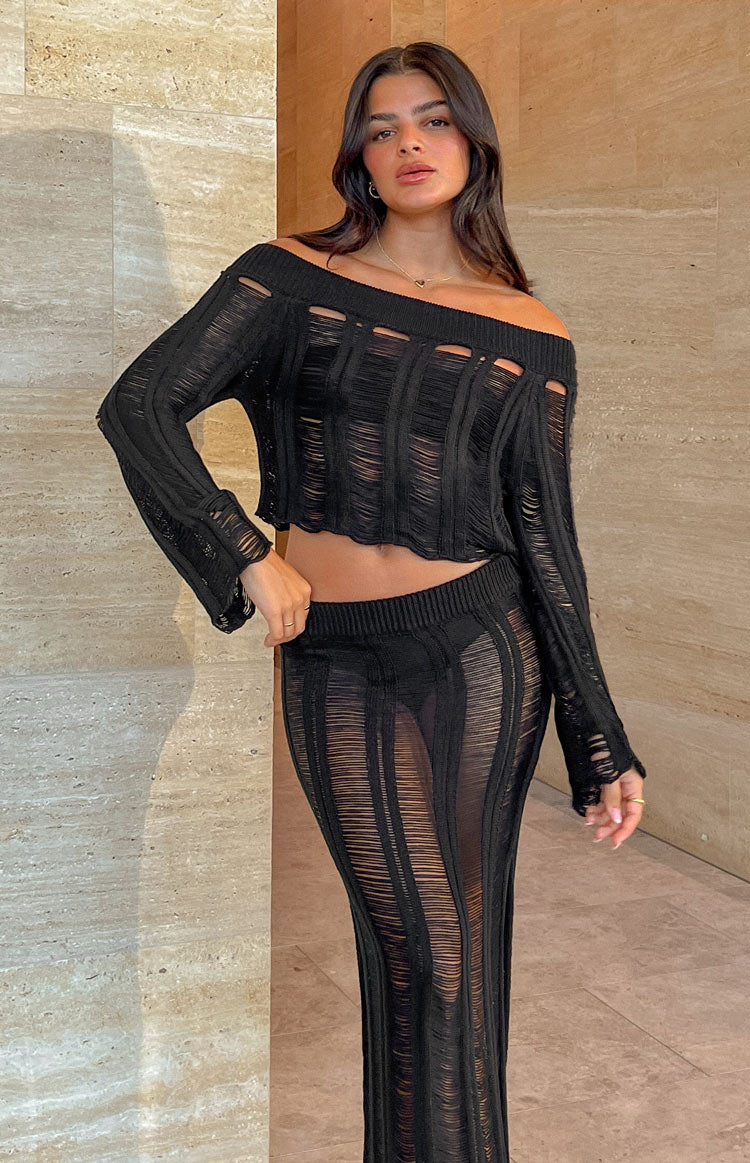 Brunette model is posed front on wearing a cropped, long sleeve, black, ladder knit top.