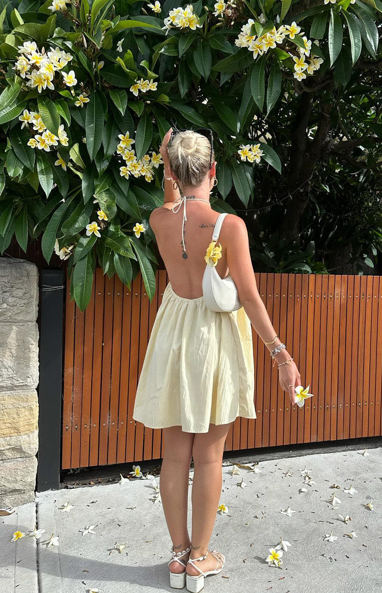 Rear view of a yellow mini dress showing the halter neck ties and low open back with a gathered waist