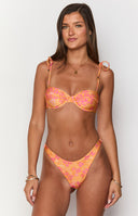 Girl wearing orange bikini top and bottoms with gold jewellery in front of pool chair.