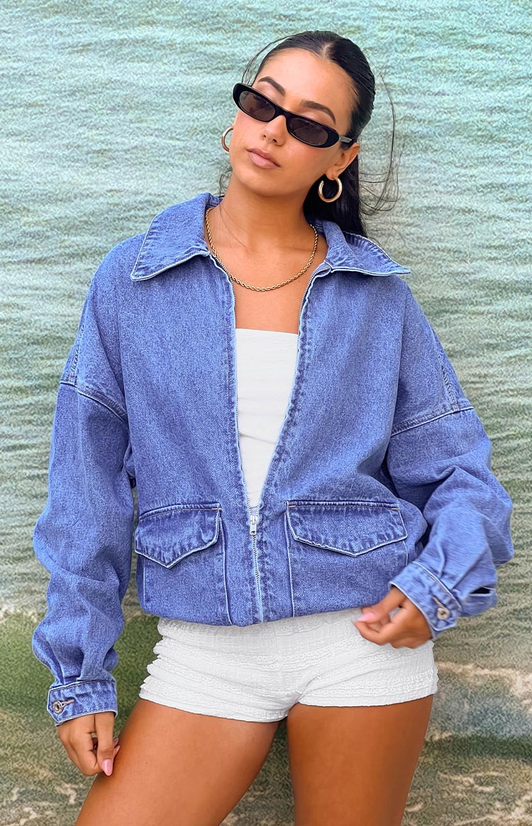 Front view of a mid wash denim bomber jacket with a wide collar, full zip, and two large flap pockets