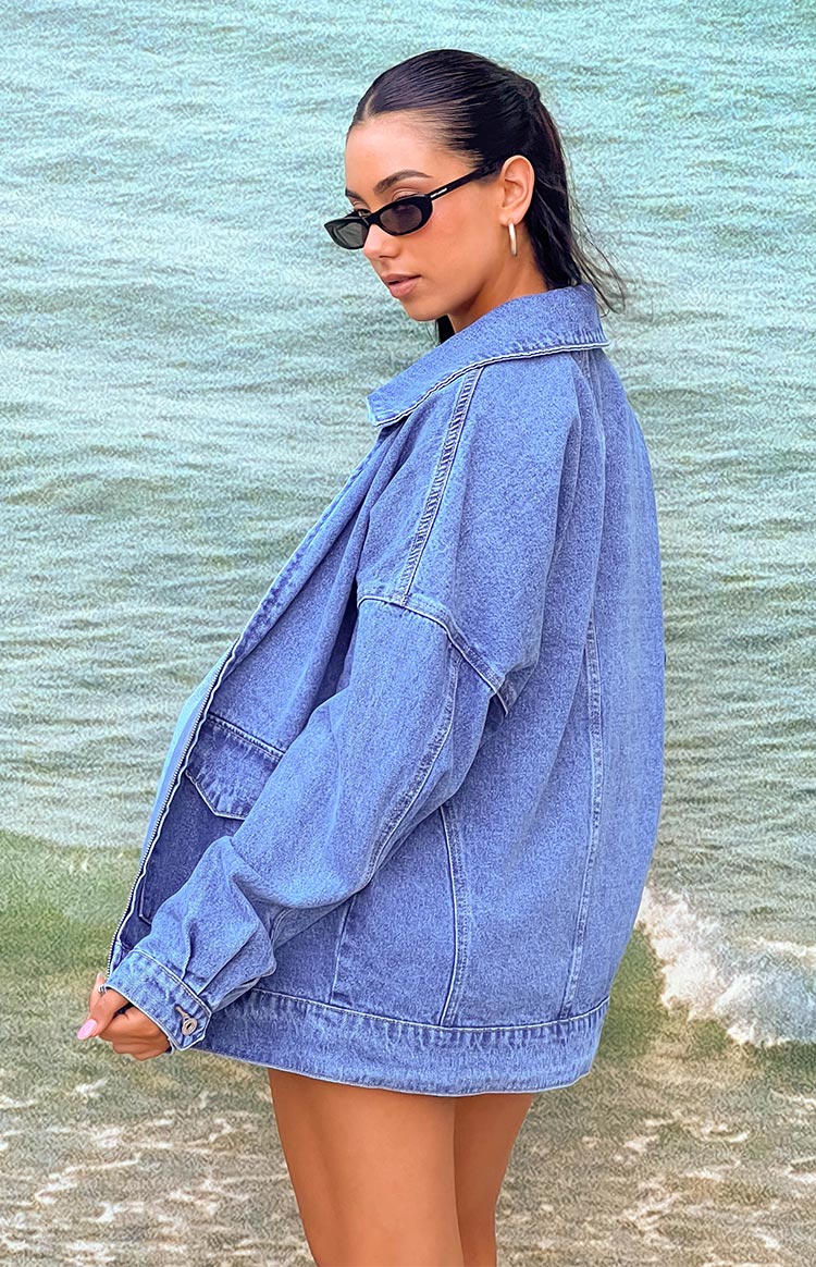 Model wearing oversized denim jacket with black sunglasses in front of ocean photo