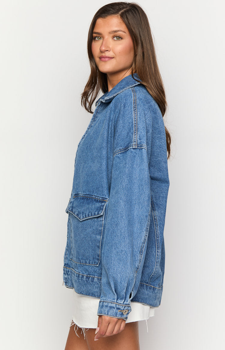 Side view of a mid wash denim bomber jacket with a relaxed fit, dropped shoulders, and large flap pockets