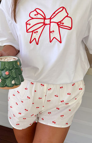 Close-up of white pajama shorts with a scattered red cherry print and relaxed fit