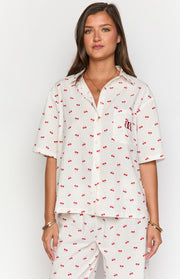 White short sleeve pajama shirt with red cherry print, collared neckline, and chest pocket with embroidered logo