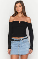 Brunette model wearing a black long sleeve off shoulder top, denim mini skirt and gold jewellery holding a drink
