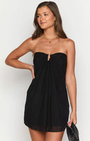 Brunette girl wearing a black strapless mini dress and gold jewellery holding a drink.