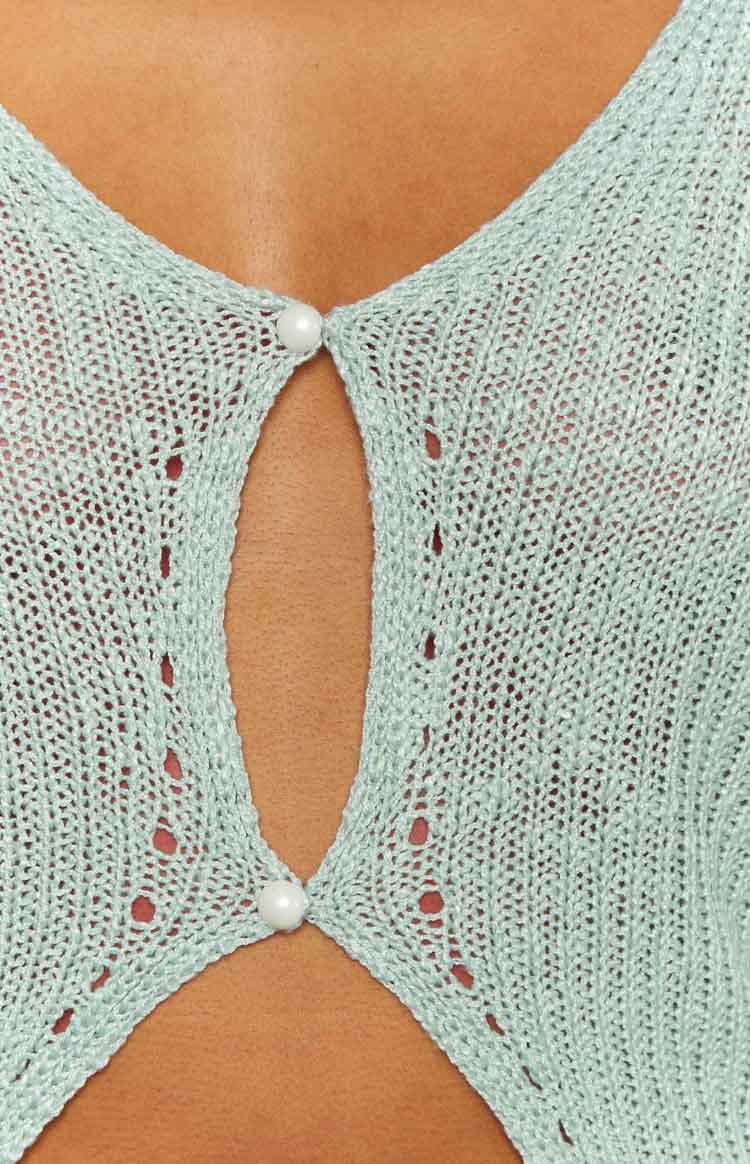 Close-up of the light blue knit top showing the pearl button closure, keyhole cutout, and open knit pattern