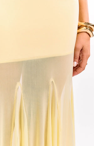 A close-up of a yellow maxi-dress highlighting the transition from the solid fitted bodice to the sheer flowing skirt panel with distinct scalloped seams.