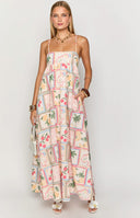 blonde model wearing a babydoll style maxi dress with an italian themed print paired with tan sandals
