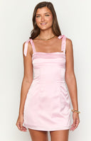 blonde model wearing a pink satin mini dress with adjustable bow details on straps