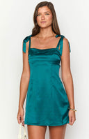 blonde model wearing a teal satin mini dress with adjustable bow straps and pin tuck bust details