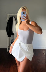 Front view of a white denim asymmetrical wrap mini skirt with a single button closure and front pockets