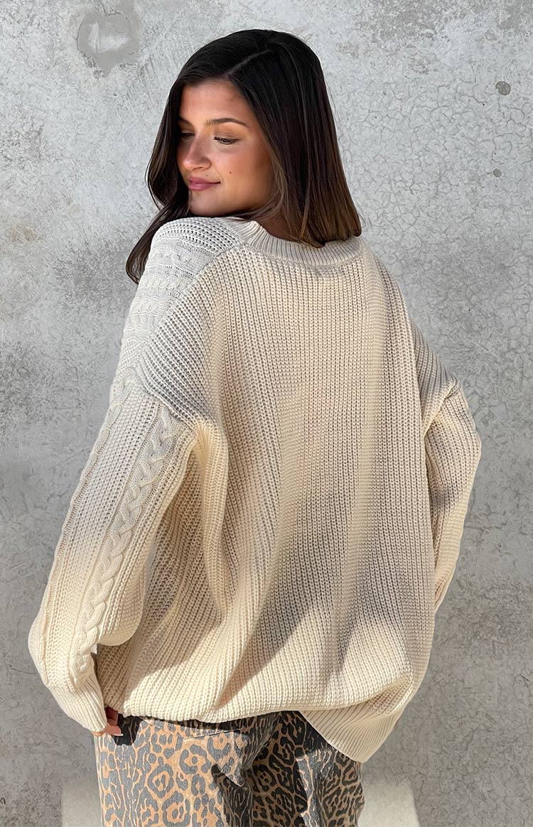 Rear view of a cream oversized sweater with ribbed knit body and cable knit details on the sleeves and shoulder