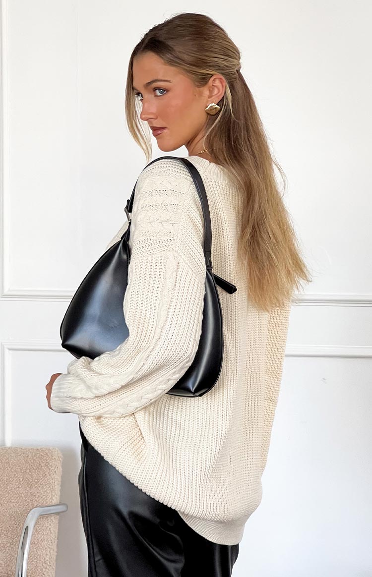 Side view of a cream oversized sweater showing cable knit sleeves and ribbed body