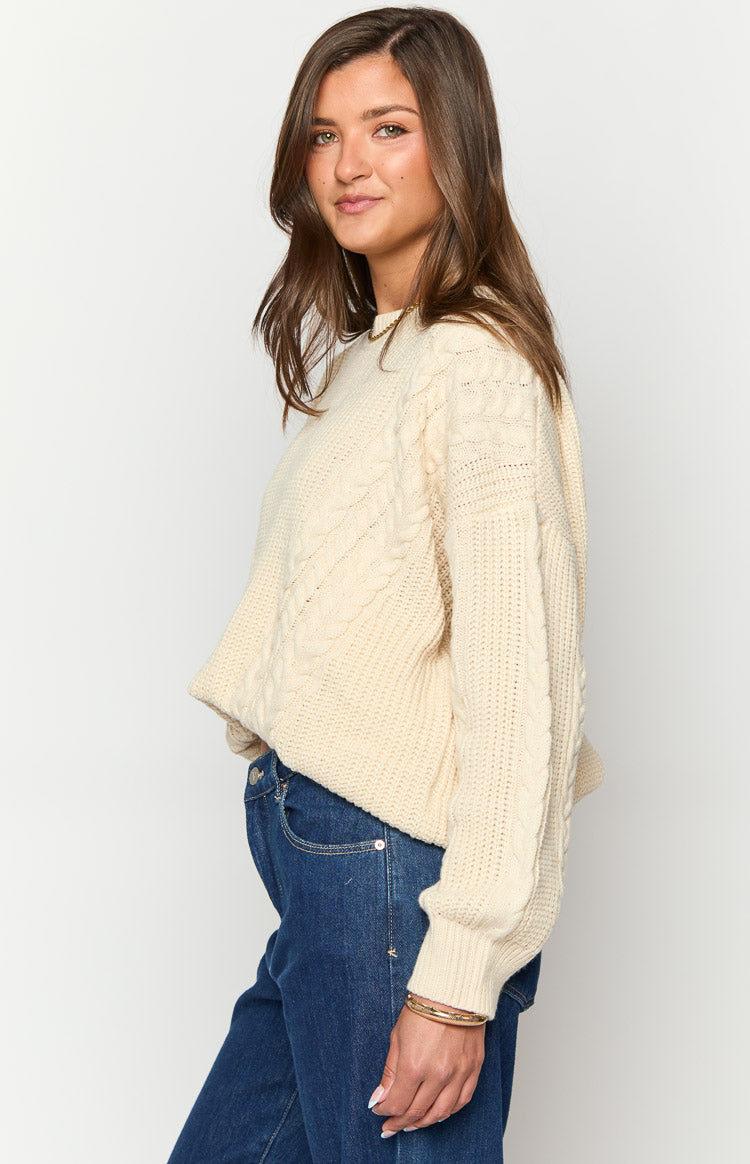 Side view of the cream oversized sweater, highlighting the chunky cable knit texture and ribbed cuffs