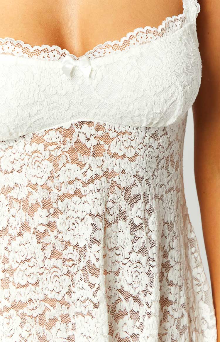 Close-up of the white floral lace mini dress showing the scalloped trim, small bow, and sheer fabric