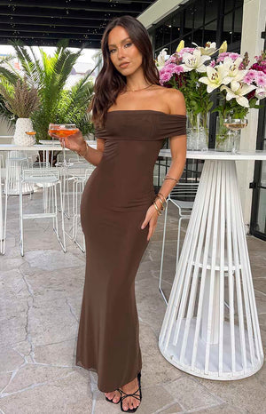 Brunette model wearing brown strapless maxi dress holding a drink at a venue.