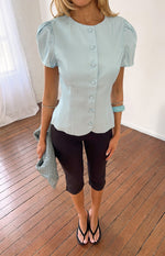 Full length view of a light blue organza button up top with puff sleeves and a scalloped hem