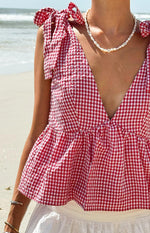 Close-up of a red gingham tie top with a deep V-neckline, tie-shoulder straps, and a gathered peplum hem