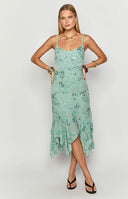 model wearing a teal midi dress with floral bead embellishments styled with a white handbag and tan heels