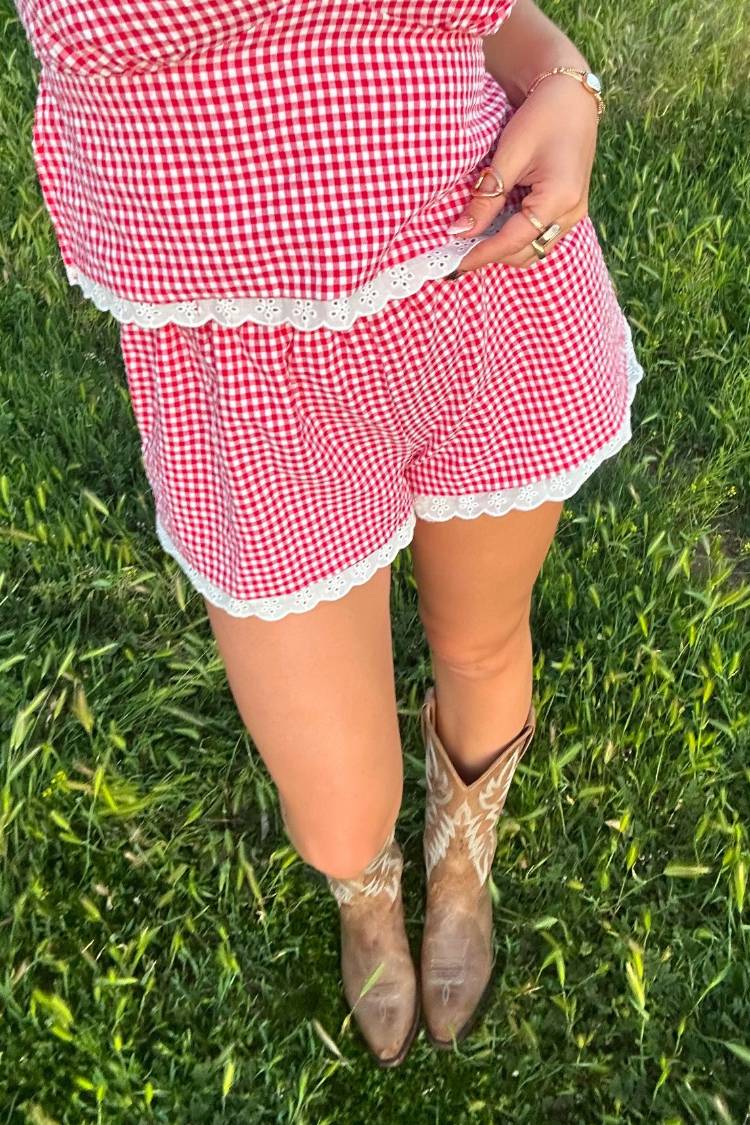 Top-down view of red gingham shorts with white broderie lace trim on the hem and waist