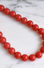 Close-up showing the vibrant red, glossy finish of the round beaded necklace