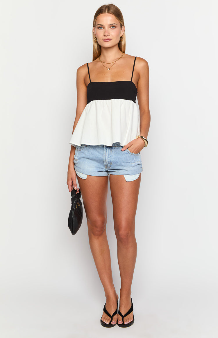 Front view of a black and white contrast top with thin spaghetti straps and a gathered peplum hem