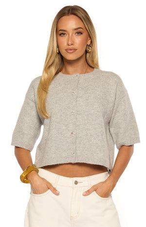 Woman in a soft light grey short sleeve cropped cardigan with button details a cozy layer for a Spring day or casual office look