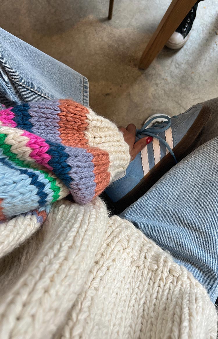 Cream ribbed knit cuff and multi-coloured striped chunky knit sleeve of a cardigan