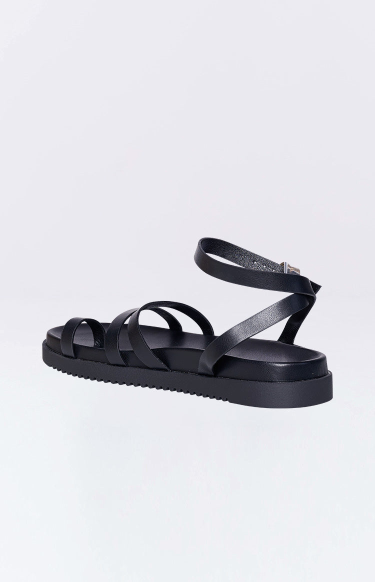Rear side view of black flat sandals showing the adjustable ankle strap with a silver buckle and a ridged platform sole
