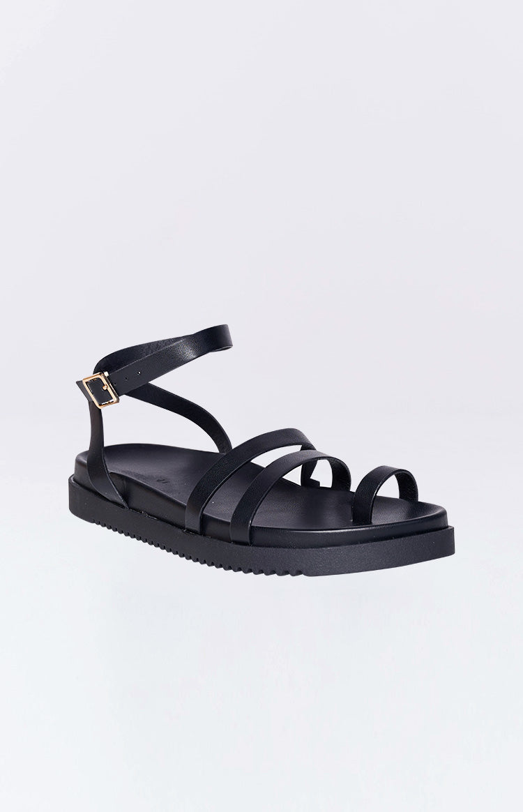 Black flat sandals with a toe ring and adjustable ankle strap with a gold buckle