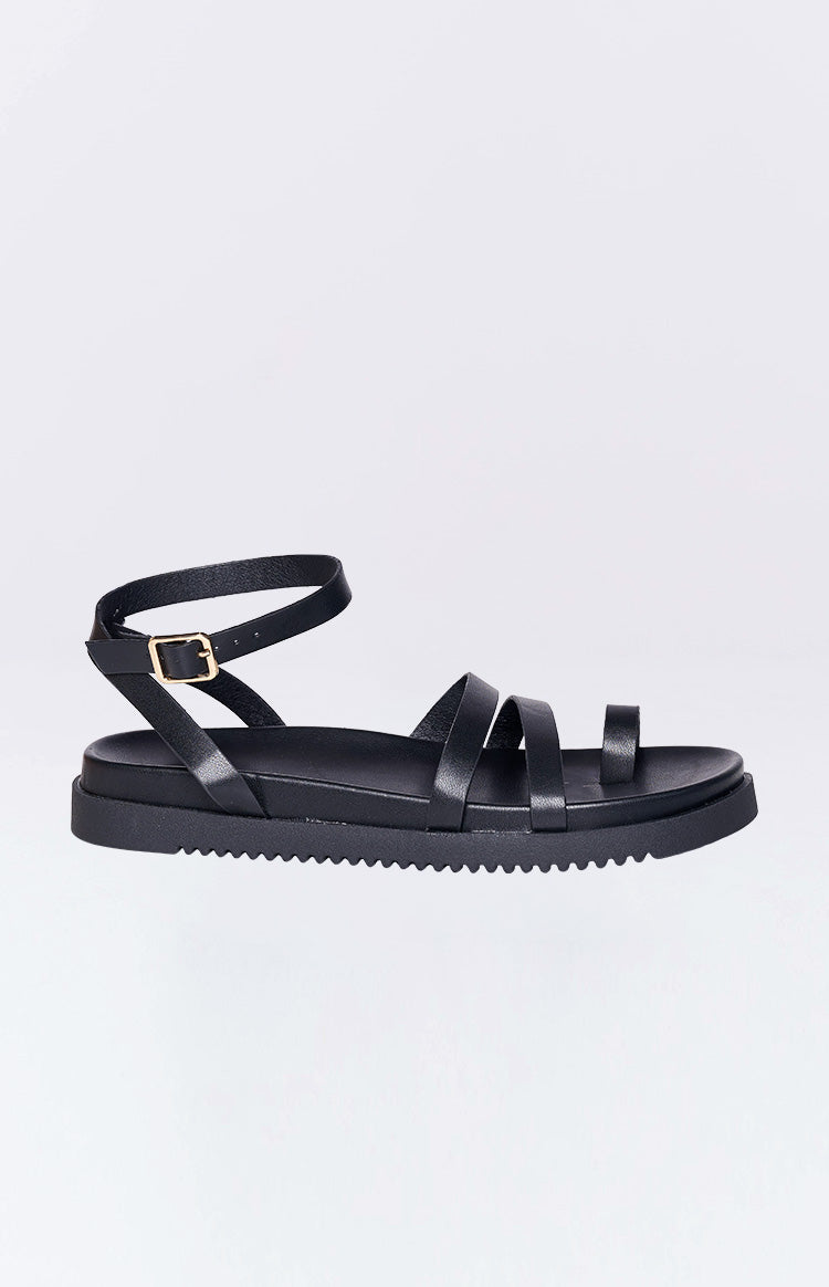 Side view of black sandals showing the ankle strap with a gold buckle and the thick ridged sole