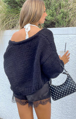Rear view of a black chunky knit cardigan worn off-shoulder, showing its relaxed fit and long sleeves