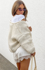 Rear-side view of a cream chunky knit cardigan with an oversized fit, dropped shoulders, and visible texture