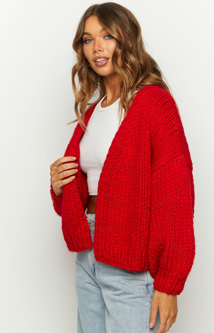 Angled view of a red chunky knit cardigan with an open front and ribbed cuffs