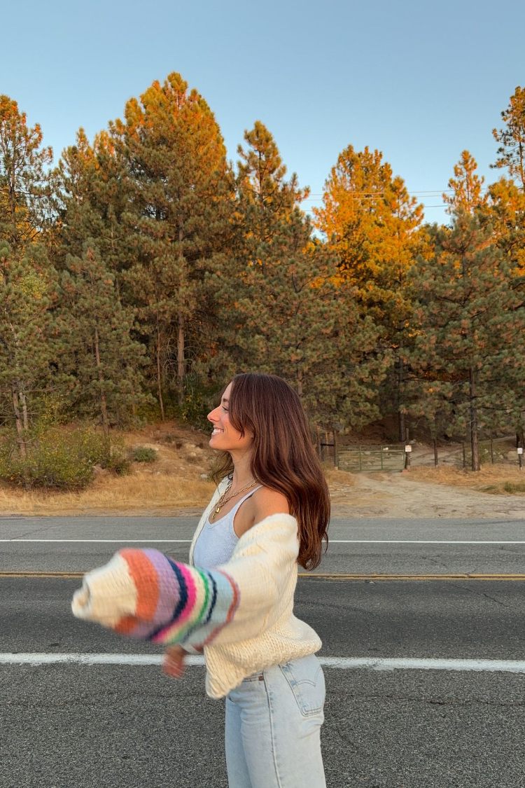 Side view of a cream chunky knit cardigan with voluminous multi-coloured striped sleeves