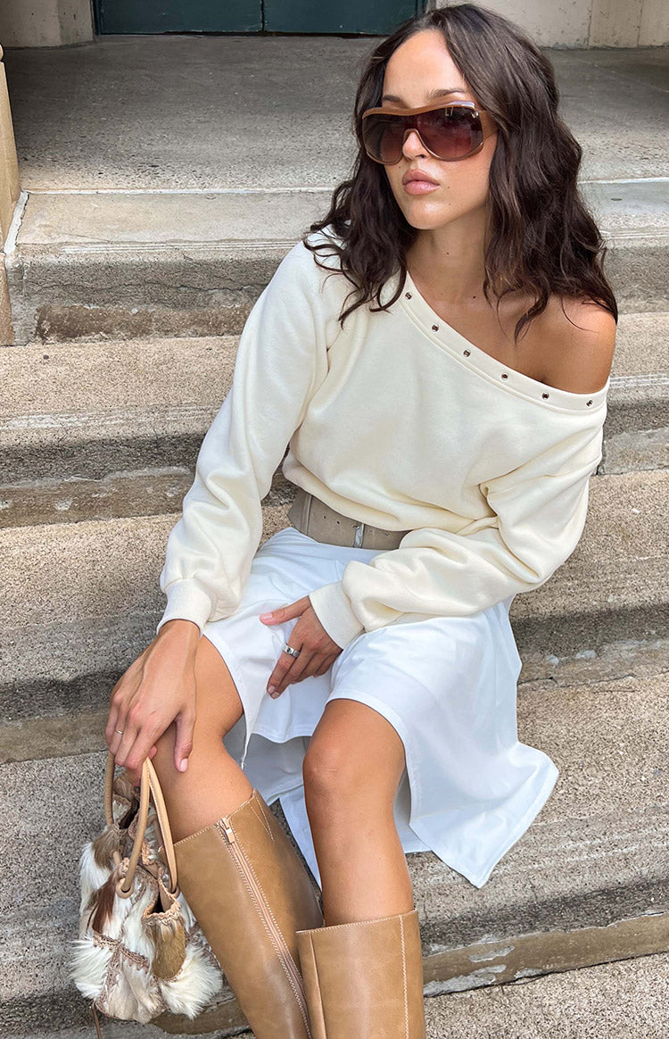 Side view of cream asymmetric neckline sweater with eyelets, styled off-shoulder to show the relaxed fit