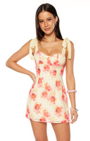 Our model wearing a light yellow mini-dress with a pink and coral abstract floral print featuring a sweetheart neckline with underwire cups and tie-up shoulder straps.
