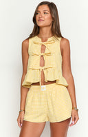 a girl with blonde hair wears a yellow and white gingham top with bows and a matching pair of boxer shorts and a gold bracelet