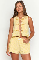 a model holds a coffee cup while wearing a yellow gingham top with bows and a matching pair of boxer shorts