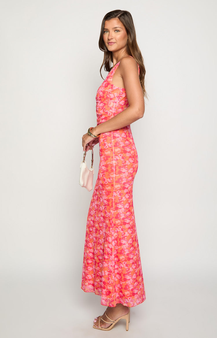 Side view of an orange and pink floral print maxi dress with a fitted ruched bodice and a flowy A-line skirt