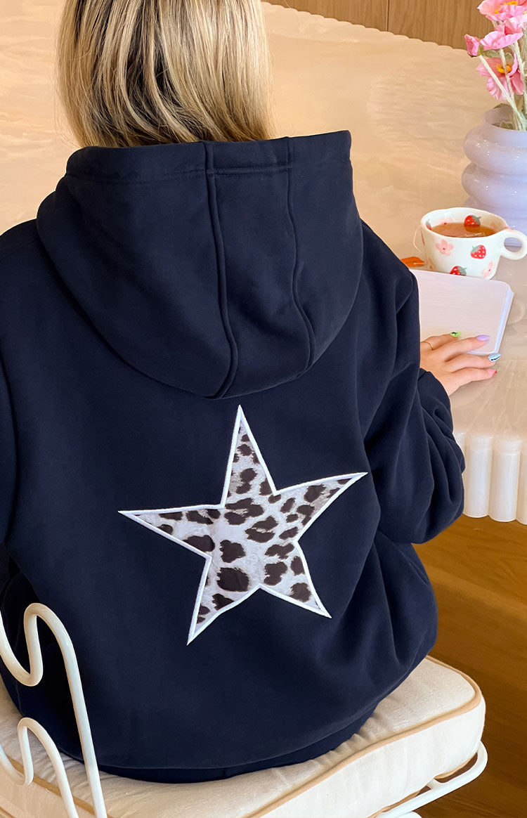 The back view of a navy blue hoodie featuring a large white star appliqué with a cow print pattern on the back.