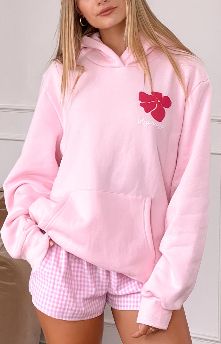 blonde model wearing a baby pink hoodie with a pink flower graphic detail and front pocket