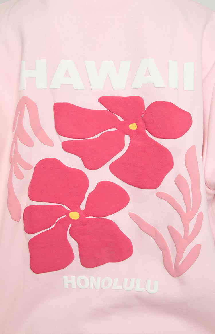 Close-up of the pink hoodie's graphic print featuring white 'HAWAII' text, two dark pink hibiscus flowers, and 'HONOLULU' tex
