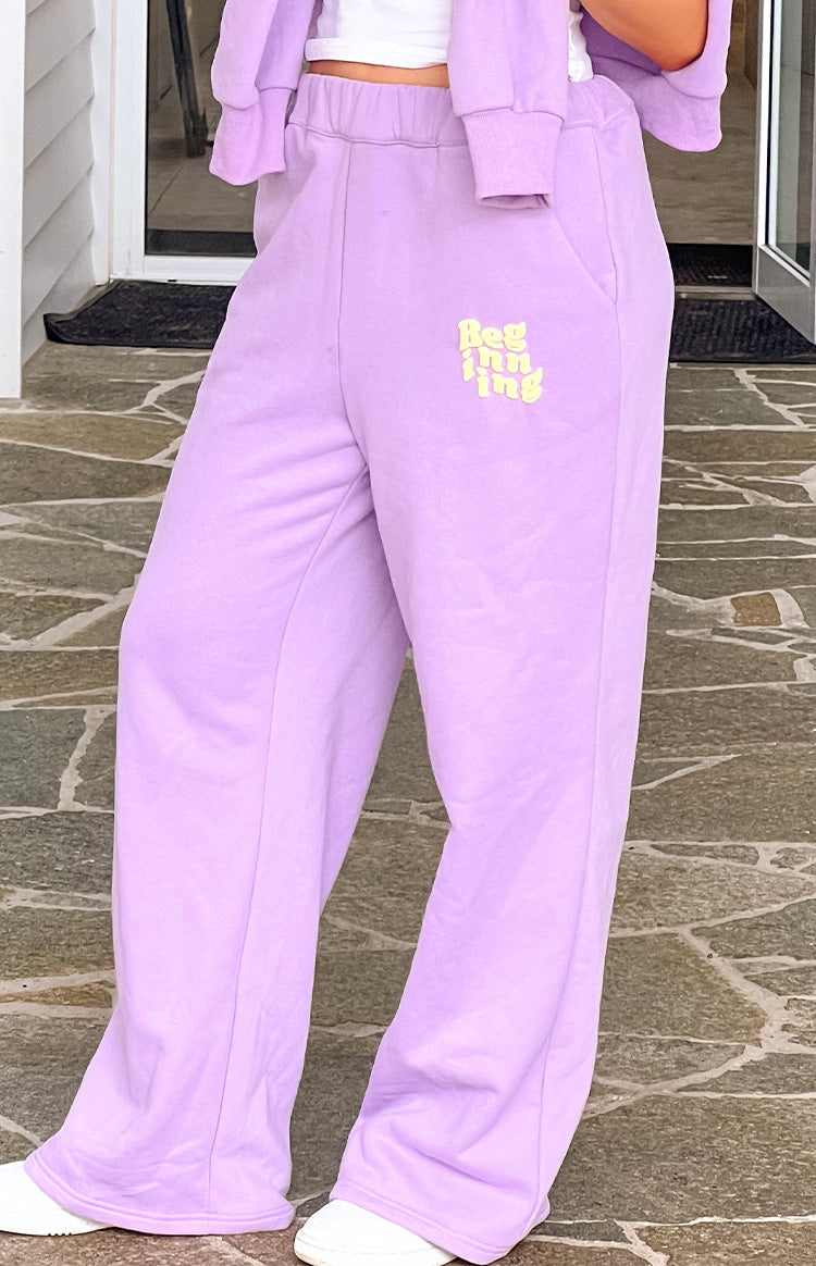 Angled view of purple wide-leg track pants with an elasticated waist, yellow 'Beginning' logo, and vertical front seams