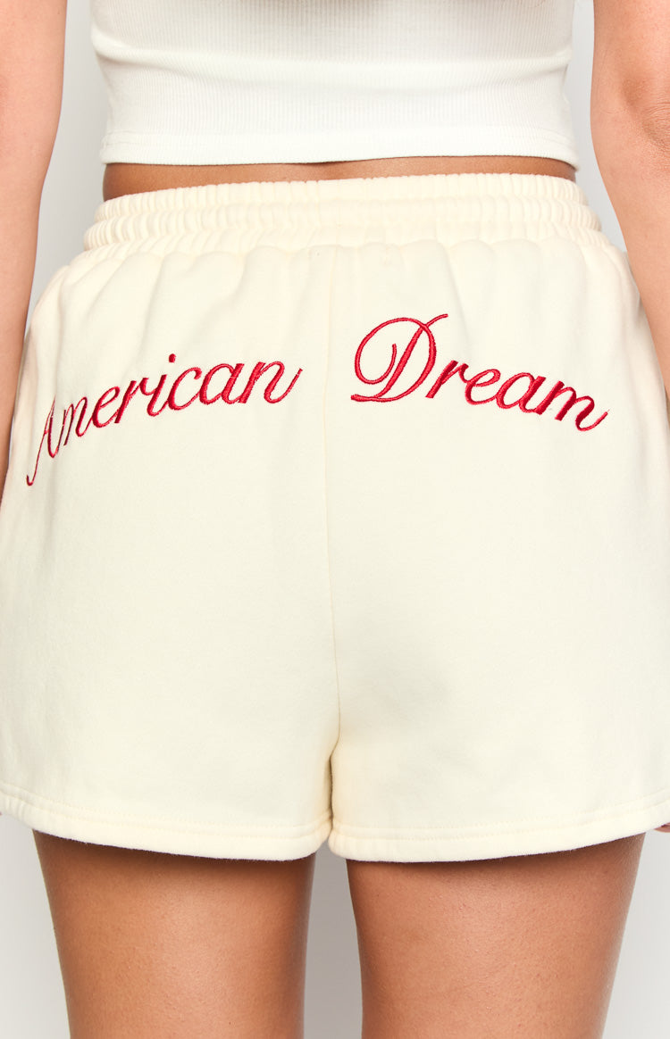 Close-up back view of cream fleece lounge shorts with red 'American Dream' script embroidery and elasticated waistband