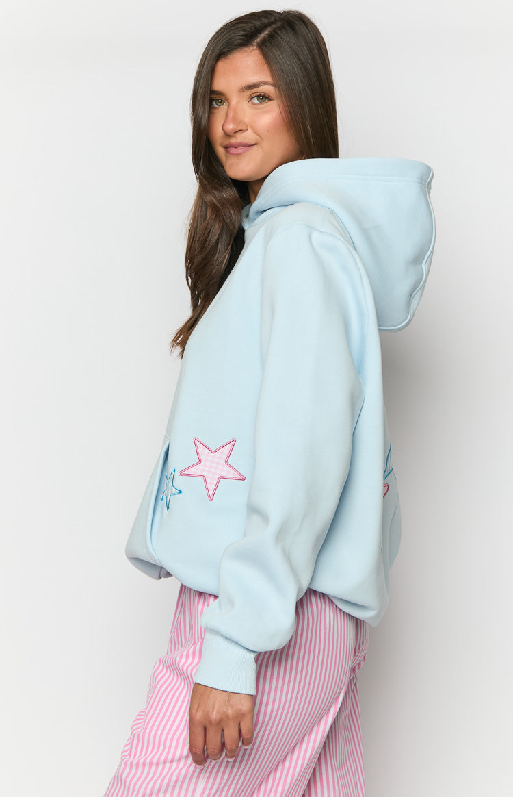 Side view of a light blue hoodie with a pink gingham star patch and a blue star outline on the side, showing the hood and rib