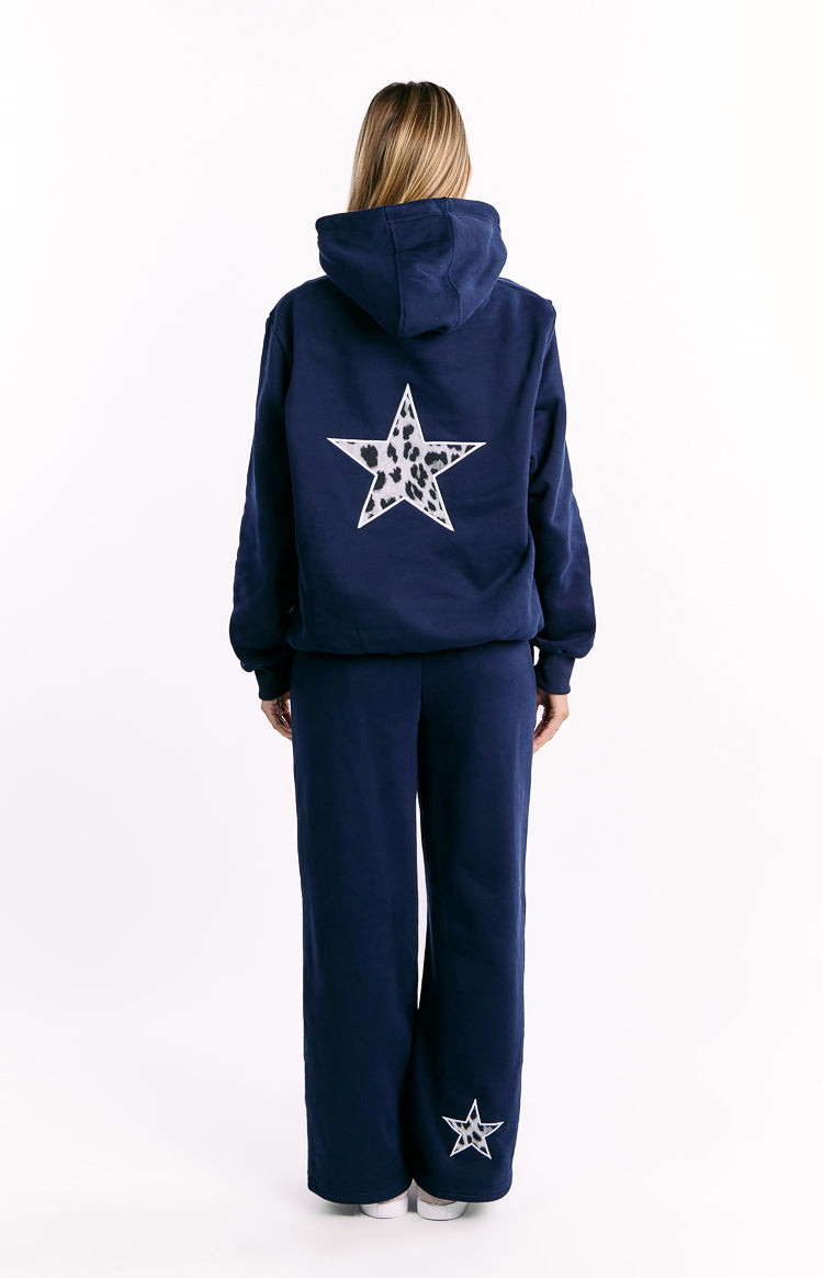 Rear view of a navy hoodie with a large white leopard print star on the back, and matching navy wide-leg pants with a small star