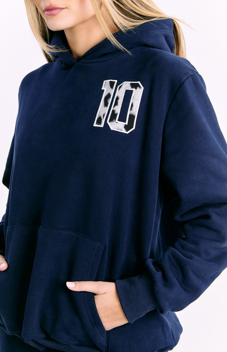 Close-up of the navy hoodie showing the black and white animal print '10' patch, front kangaroo pocket, and ribbed cuff